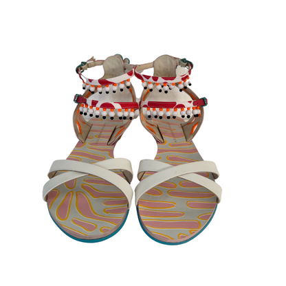 Sandalo piatto in pelle bianca con due cinturini alla caviglia con perline bianche e ricami colorati.                        